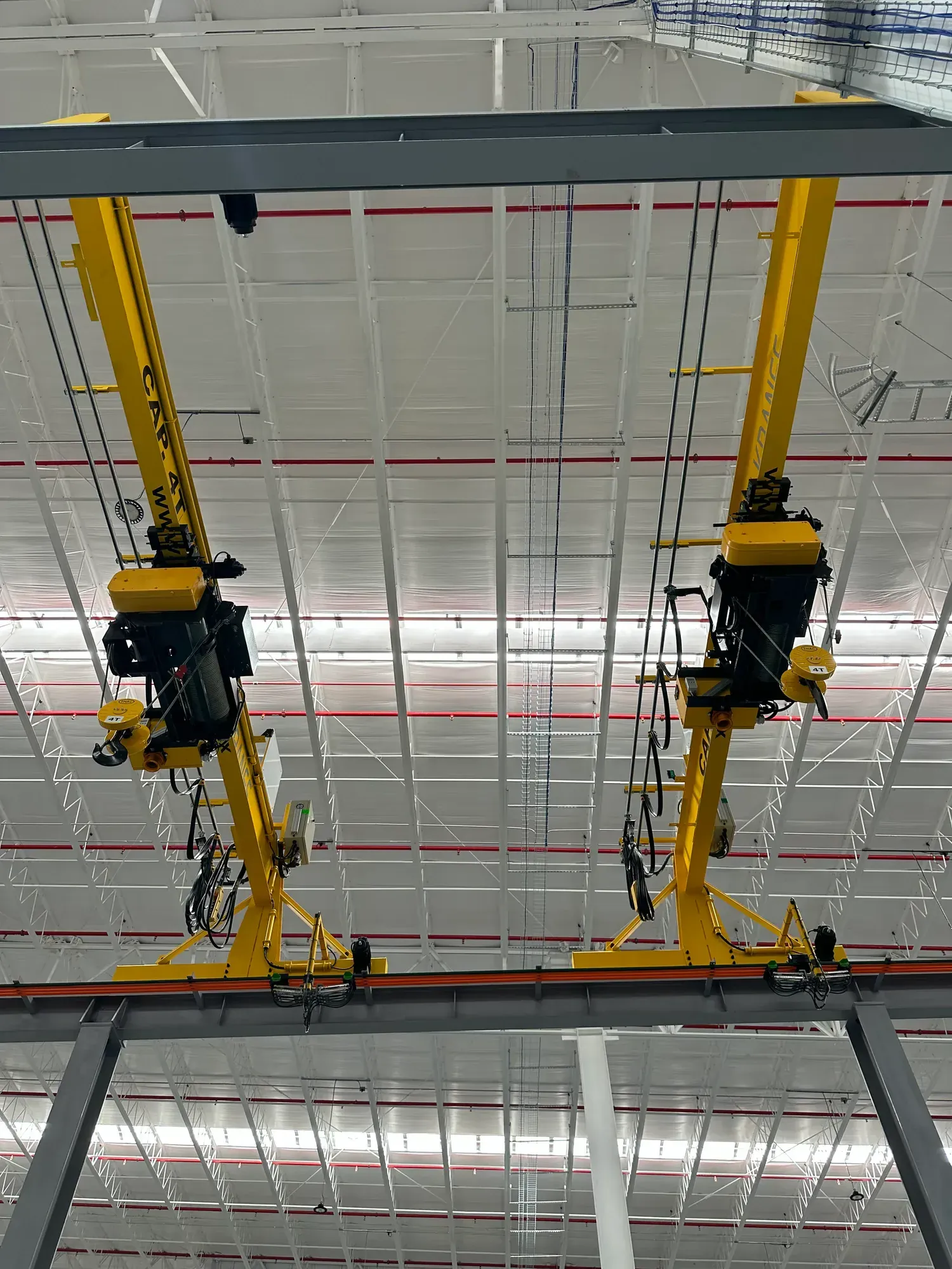 Vista inferior de dos grúas viajeras monopuente con polipastos instaladas en una nave industrial