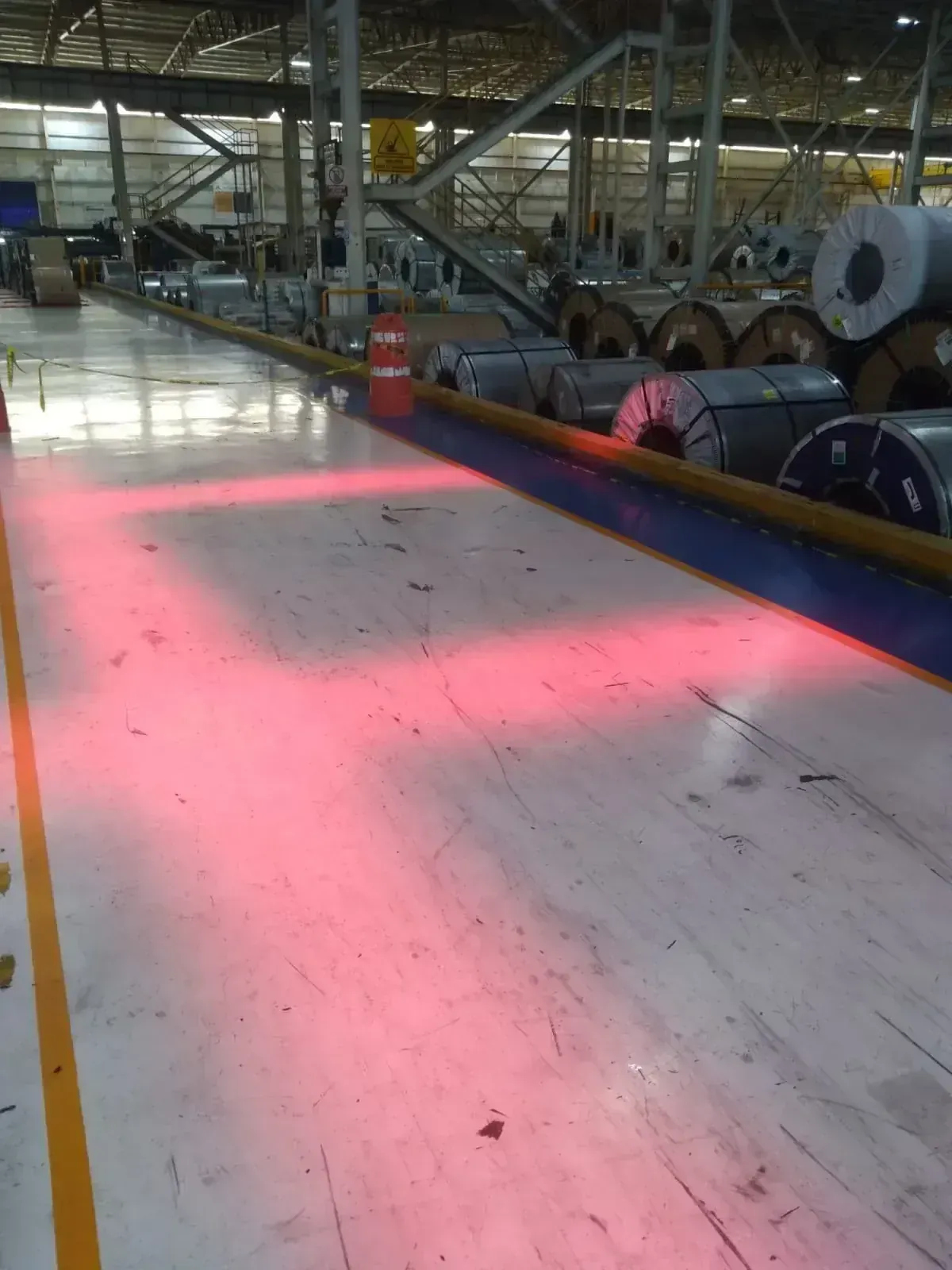 Proyección lineal roja de seguridad sobre el piso de un área industrial con bobinas de acero